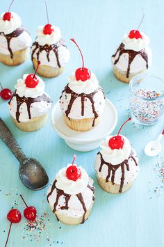 cupcakes with white frosting and cherries are on a blue tablecloth