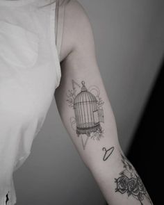 a woman's arm with a birdcage and roses tattoo on the left arm