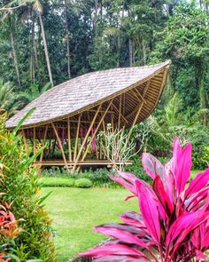 a large wooden structure in the middle of some trees and bushes with purple flowers around it