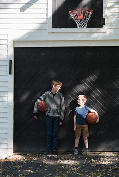 two young boys standing in front of a garage door holding basketballs