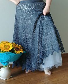 a woman standing next to a vase with sunflowers in it and wearing a skirt