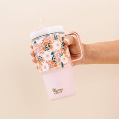 a hand holding a pink coffee cup with flowers on it and a straw in the cup