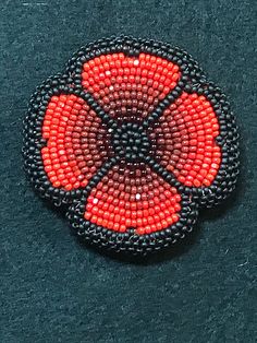 a red and black beaded brooch sitting on top of a blue cloth covered surface