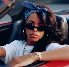 a woman sitting in the driver's seat of a car wearing sunglasses and a head scarf