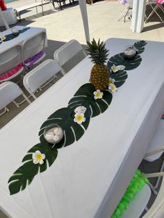 a pineapple sits on top of a table with white chairs and green decorations around it