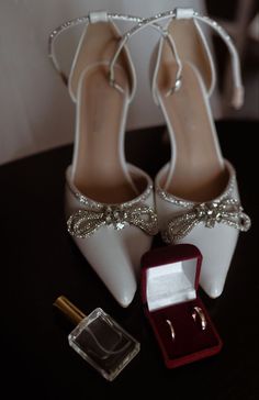 a pair of white high heels sitting on top of a table next to a ring