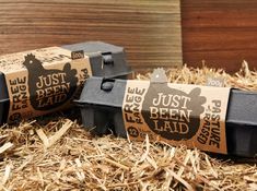 two black boxes with labels on them sitting in some hay and straw next to a wooden wall