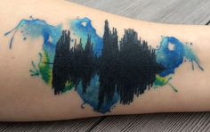 a person with a tattoo on their arm that has blue and green paint splattered on it