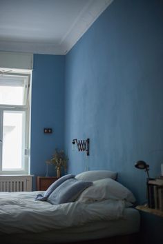 a bed sitting in a bedroom next to a window with blue walls and white sheets