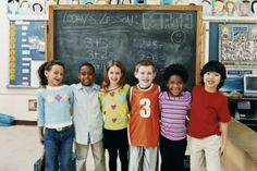 a group of children standing in front of a blackboard with writing on it and smiling at the camera