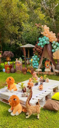 an outdoor party with balloons and stuffed animals on the grass, including giraffes