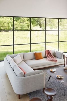 a living room filled with furniture and large windows next to a grass covered field in the background