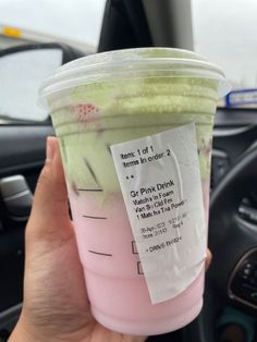 a person holding up a pink and green drink in their hand with the label on it