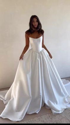 a woman wearing a white wedding dress standing in front of a wall with her hands on her hips