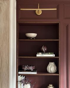 a book shelf with books and vases on it in front of a red wall