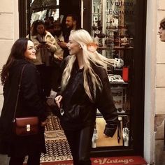 two women are standing in front of a store door talking to each other while others look on