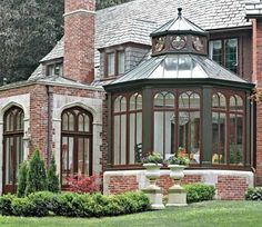 a large brick house with many windows and plants in the front garden area, surrounded by lush green grass