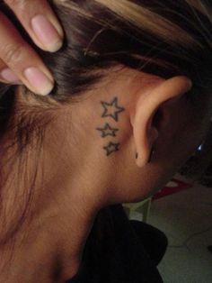 a woman with a small star tattoo on her left side behind the ear is looking down