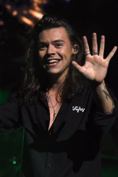 a man with long hair and piercings waves to the crowd while holding his hand up