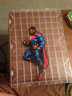 a cross - stitch picture of a man in a blue suit and red cape sitting on top of a table