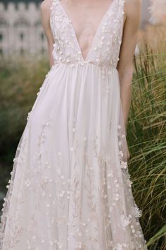 a woman in a white dress standing next to some tall grass and flowers on her head