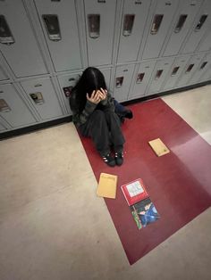 a person sitting on the floor in front of lockers with their hands to their face