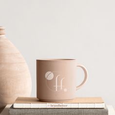 a pink coffee mug sitting on top of a book next to a vase and pottery