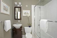 a white toilet sitting next to a walk in shower under a bathroom mirror above a sink