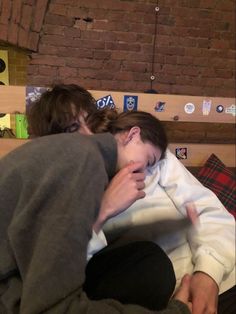 two people sitting on a bed with one person covering their face and the other holding his head