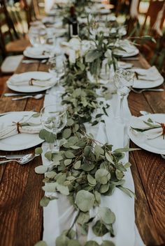 the table is set with white plates and greenery