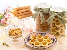 small cookies in glass jars and plates on a table with flowers, candles and other items