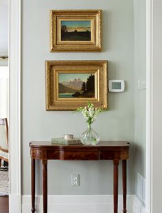 two paintings hang on the wall above a table with vases and flowers in it