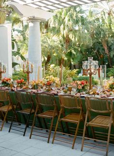 a long table is set up for an outdoor event with tall candles and floral centerpieces