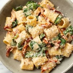 a bowl filled with pasta and spinach covered in sauce on top of a marble table