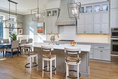 a large kitchen with an island and bar stools in the center, surrounded by gray cabinets