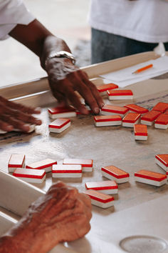 two hands reaching for pieces of red and white paper on top of a metal surface