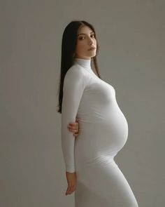 a pregnant woman posing for the camera with her hands on her hips, wearing a white dress