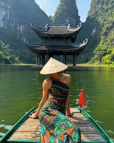 a woman wearing a hat sitting on top of a boat in front of a mountain