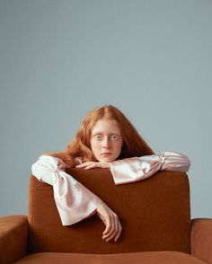 a woman with long red hair sitting on a brown couch and looking at the camera