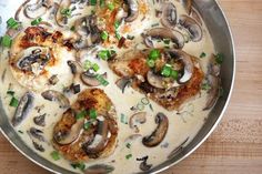 a pan filled with meat covered in mushrooms and green onions on top of a wooden table