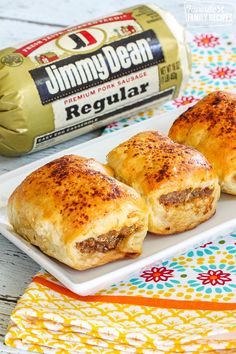 two sausage rolls on a white plate next to a bottle of beer and napkins