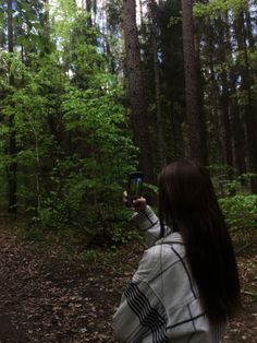 a woman standing in the woods taking a photo with her cell phone