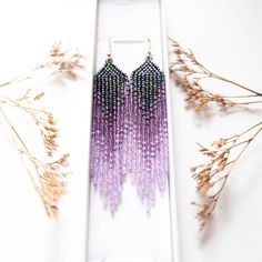 purple and blue beaded earrings sitting on top of a white box next to dried flowers