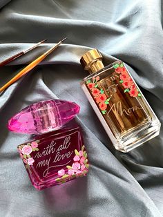 two perfume bottles sitting on top of a bed next to an artist's palette