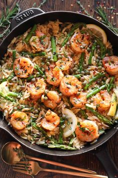 shrimp, asparagus and rice in a skillet on a wooden table with utensils