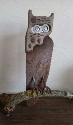 an owl statue sitting on top of a tree branch with eyes painted on it's face