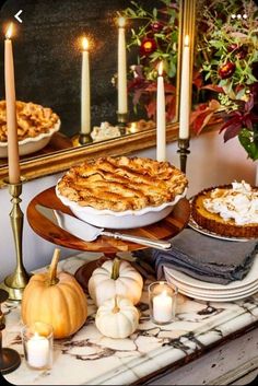 a table topped with pies and pumpkins next to candles in front of a mirror