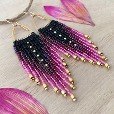 purple and black beaded earrings with gold accents on a wooden table next to pink flower