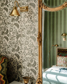 a bedroom with green and white wallpaper, gold framed mirror and bed in the corner