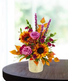 a bouquet of flowers sitting on top of a wooden table next to a vase filled with purple and orange flowers